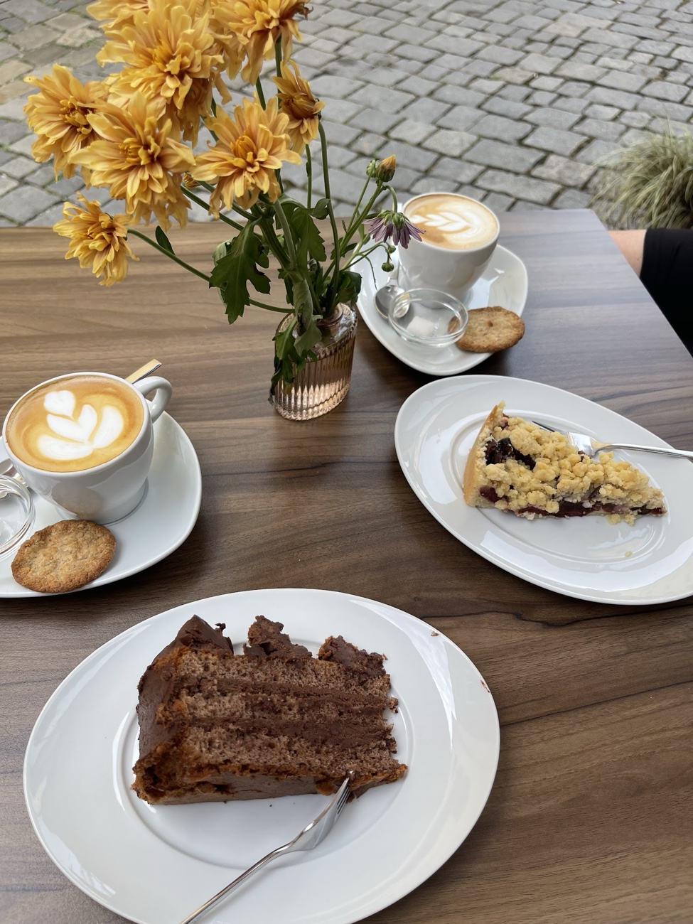 Schokoladentorte und Streuselkuchen mit zwei Cappuccini auf dem Tisch vor dem Café